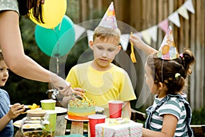 Cute funny nine year old boy celebrating his birthday with family or friends and eating homemade baked cake in a backyard.