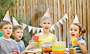 Cute funny nine year old boy celebrating his birthday with family or friends with homemade baked cake in a backyard. Birthday