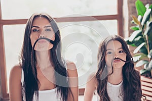 Cute funny sisters with beautiful long hdark hair are making fake mustache with their hair, they are having fun