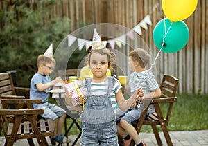 Cute funny six year old girl celebrating her birthday with family or friends in a backyard. Birthday party. Kid wearing party hat