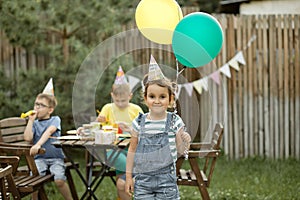 Cute funny six year old girl celebrating her birthday with family or friends in a backyard. Birthday party. Kid wearing party hat