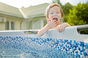 Cute funny toddler boy having fun by an outdoor pool. Kid playing with water. Family fun in a pool. Summer activities for the