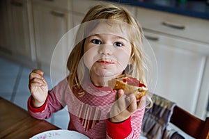 Cute funny toddler girl eats sweet bun for breakfast. Happy child eating bread roll with strawberry jam. Health food for