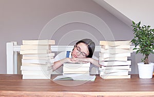 Cute funny tween girl in glasses tired of reading and studying sleeping peacefully with her head on books between stack of books