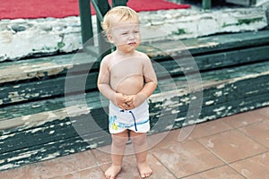 Cute funny upset caucasian 2 year old toddler boy standing abandoned alone at beach summer day. Offended scared child