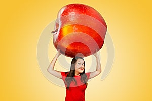 Cute funny young girl holds over herself huge red apple on a orange background