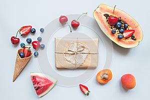 Cute gift box wrapped with craft paper and summer fruits top view. Summer gift