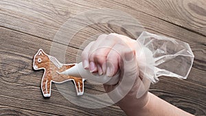 Cute gingerbread horse and human hand with piping bag on brown wooden background