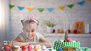 Cute girl admiring colorful eggs, preparing for Easter Sunday, happy childhood photo