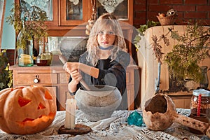 Cute girl age 10 years old in a witch costume in an old house on Halloween, brews a potion and conjures.