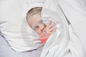 cute girl in a bathrobe with a hood after a shower hides under the covers and has fun