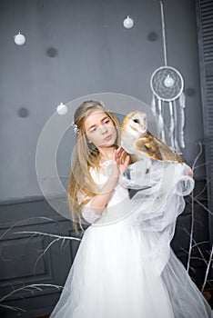 Cute girl with blond hair in a white dress with a white owl