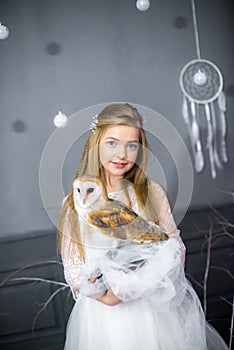 Cute girl with blond hair in a white dress with a white owl