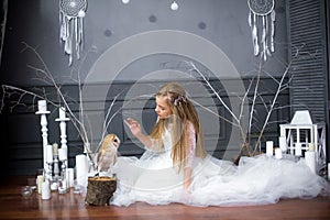 Cute girl with blond hair in a white dress with a white owl