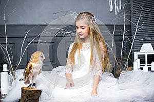 Cute girl with blond hair in a white dress with a white owl