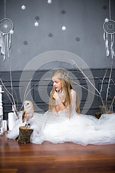 Cute girl with blond hair in a white dress with a white owl