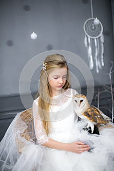 Cute girl with blond hair in a white dress with a white owl