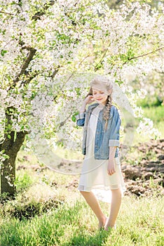 Cute girl with blond hair in a white sundress in spring