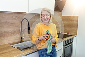 Cute girl with blond red hair whipping her apple with kitchen towel. Young Woman cleaning her fruit in her kitchen. Daily intake