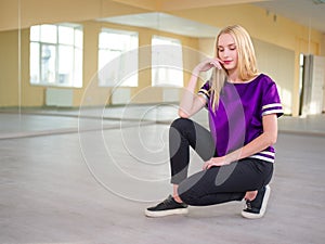 Cute girl, blonde, sitting posing in a light dance studio.