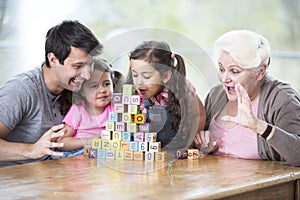 Cute girl blowing alphabet blocks while family looking at it in house