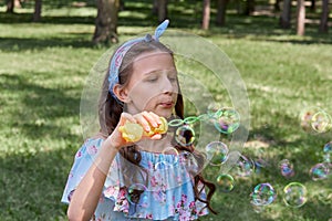 Cute girl in blue dress blowing soap bubbles in summer in the Park.