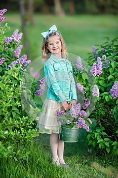 Cute girl in blue jackets with fairy airy skirt standing close to lilac bush