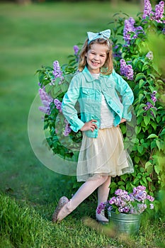Cute girl in blue jackets with fairy airy skirt standing close to lilac bush