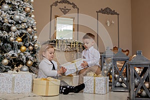 Cute Girl and boy opening Xmas presents. Children under Christmas tree with gift boxes. Decorated living room with traditional