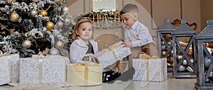 Cute Girl and boy opening Xmas presents. Children under Christmas tree with gift boxes. Decorated living room with traditional