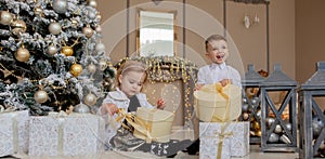 Cute Girl and boy opening Xmas presents. Children under Christmas tree with gift boxes. Decorated living room with traditional