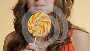 Cute girl with caramel candy on colored studio background, young happy woman have fun with sweet lollipop, concept positive mood