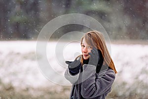 A cute girl of caucasian appearance is talking on the phone and looking at the camera on a snowy background.