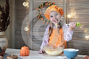 Cute girl in a chef costume is cooking pumpkin pie in the kitchen