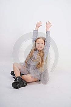 Cute girl child with long blond hair sitting on the floor and yawns sweetly, stretching her hands in different directions on white