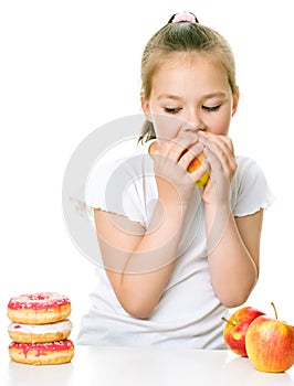 Cute girl choosing between apples and cake