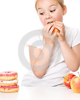 Cute girl choosing between apples and cake