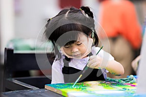 Cute girl is coloring on a canvas. Children work on watercolor art. Child wear black aprons to prevent white school uniforms from