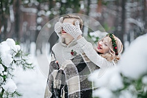 Cute girl covering boyfriend`s eyes by her knitted mittes. Winter wedding. Artwork.