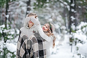 Cute girl covering boyfriend`s eyes by her knitted mittes. Winter wedding. Artwork.