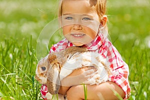 Cute girl cuddling rabbit in green field