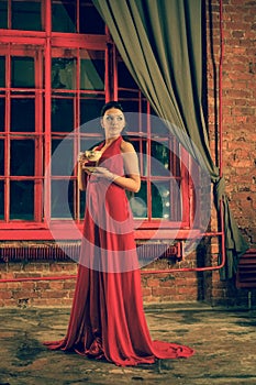 Cute girl with a Cup and a plate standing at the red big window in the evening
