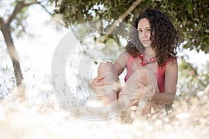 Cute girl with curly hairs sitting on the dry grass