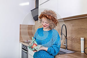 Cute girl with curly red hair whipping her apple with kitchen towel. Young Woman cleaning her fruit in her kitchen. Daily intake