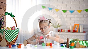 Cute girl dipping egg into glass with red food coloring, Easter traditions photo
