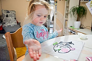 Cute girl drawing a fish using glass colors at home.