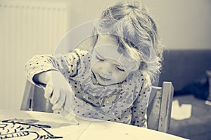 Cute girl drawing a fish using glass colors at home.