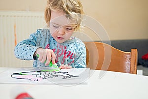 Cute girl drawing a fish using glass colors at home.
