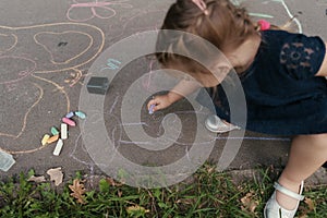 Cute girl draws on the asphalt with chalk