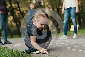 Cute girl draws on the asphalt with chalk